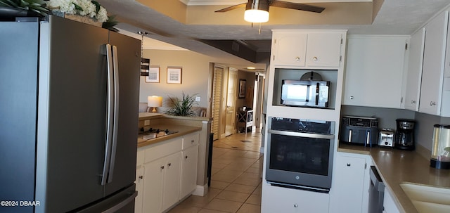 kitchen featuring ceiling fan, light tile patterned floors, a tray ceiling, white cabinetry, and stainless steel appliances