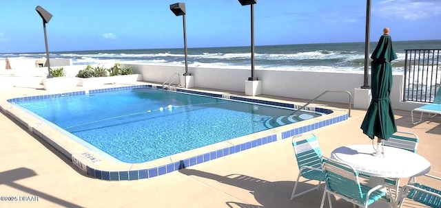 community pool featuring a view of the beach, a patio area, and a water view