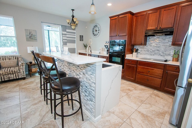 kitchen featuring under cabinet range hood, black appliances, tasteful backsplash, a kitchen bar, and pendant lighting