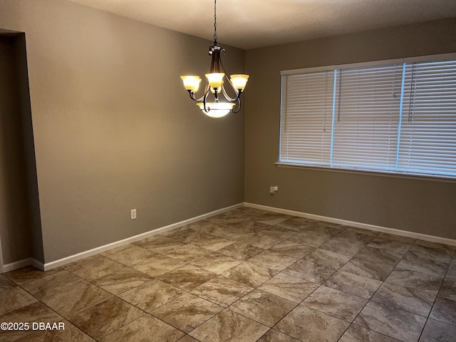 unfurnished room featuring a chandelier and baseboards