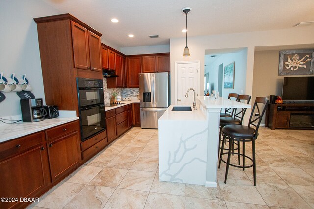 kitchen with black appliances, decorative backsplash, sink, a kitchen breakfast bar, and a kitchen island with sink