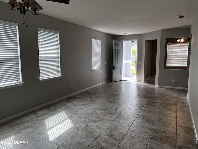 empty room with baseboards, a textured ceiling, visible vents, and a ceiling fan