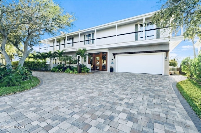 view of front facade with decorative driveway, a garage, a balcony, and stucco siding