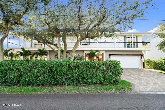 view of front facade with stucco siding, an attached garage, decorative driveway, and a balcony