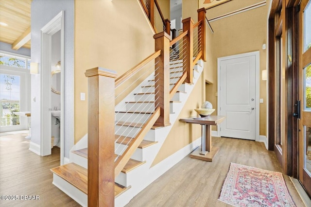 stairway featuring beam ceiling, wood finished floors, baseboards, and a towering ceiling