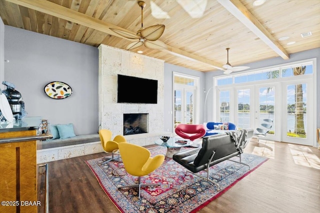 living area with beamed ceiling, a fireplace, french doors, wood finished floors, and a ceiling fan