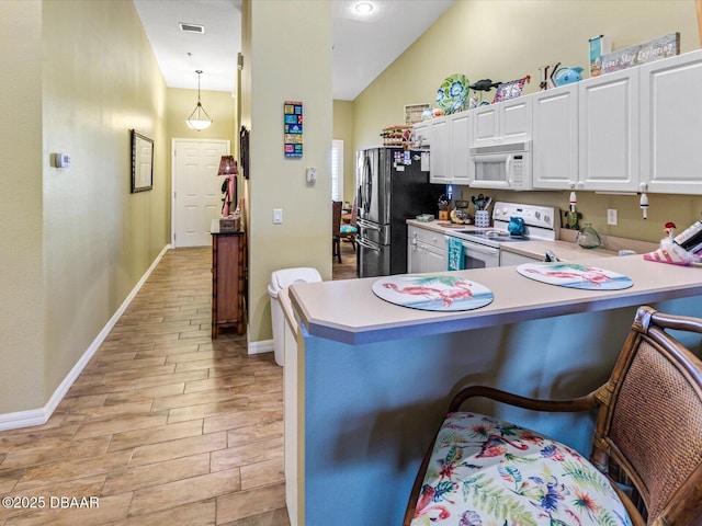 kitchen with white cabinets, light wood-style flooring, white appliances, light countertops, and a breakfast bar area