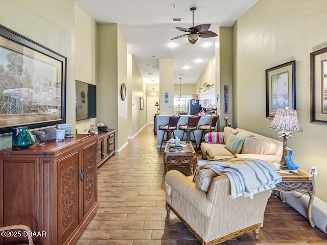 living room featuring wood tiled floor, visible vents, baseboards, and ceiling fan