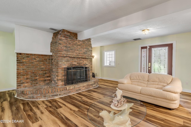 living room with hardwood / wood-style floors, beam ceiling, a textured ceiling, and a brick fireplace