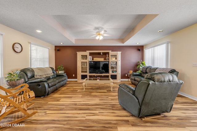 living room with a raised ceiling, ceiling fan, a textured ceiling, and light wood-type flooring