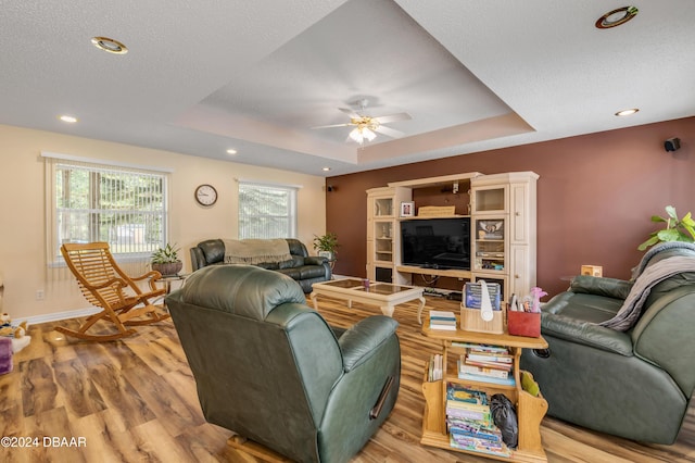 living room with ceiling fan, light wood-type flooring, a textured ceiling, and a tray ceiling