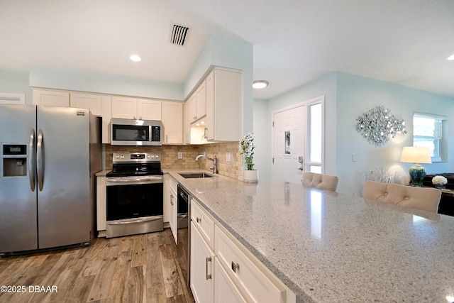 22 Sand Dune Dr, New Smyrna Beach, FL 32169 - kitchen with stainless steel appliances, light stone counters, light wood-style floors, decorative backsplash, and white cabinets