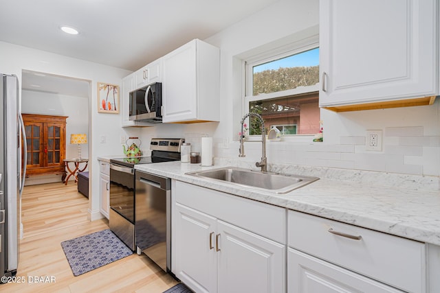 kitchen with white cabinetry, light hardwood / wood-style floors, appliances with stainless steel finishes, light stone counters, and sink