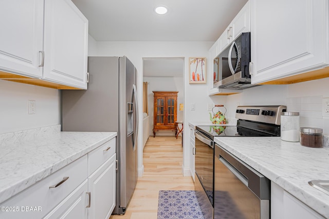 kitchen featuring light wood-type flooring, stainless steel appliances, white cabinetry, and light stone counters