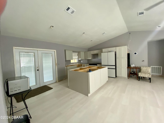 kitchen with vaulted ceiling, a kitchen island, white refrigerator, light wood-type flooring, and french doors