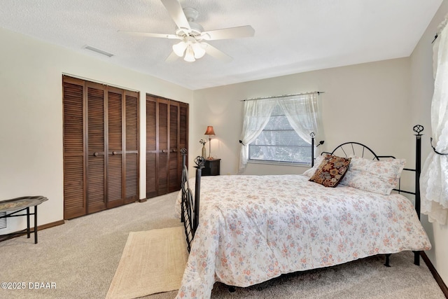 bedroom with multiple closets, ceiling fan, light carpet, and a textured ceiling