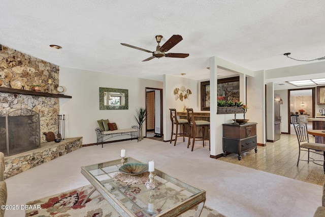 living room with ceiling fan, a fireplace, light colored carpet, and a textured ceiling