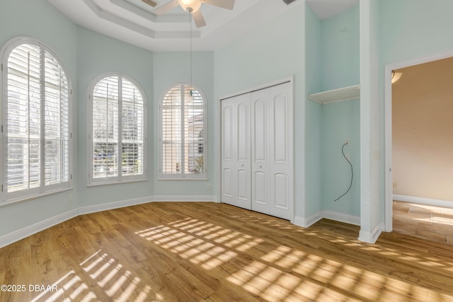 unfurnished bedroom with wood finished floors, a ceiling fan, baseboards, a closet, and a tray ceiling