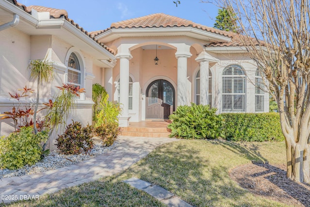 entrance to property with a tile roof, a lawn, and stucco siding