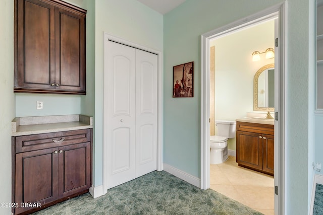 bathroom with a closet, toilet, vanity, baseboards, and tile patterned floors