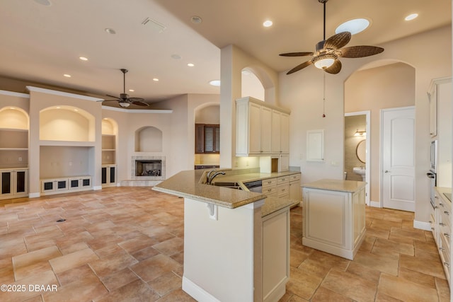 kitchen with a peninsula, a sink, built in features, cream cabinetry, and light stone countertops