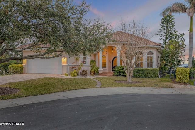 mediterranean / spanish home featuring a garage, a tile roof, decorative driveway, a lawn, and stucco siding