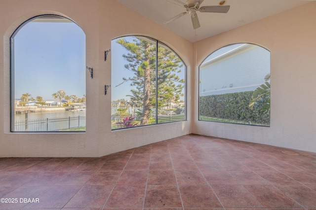 tiled spare room featuring ceiling fan and a water view