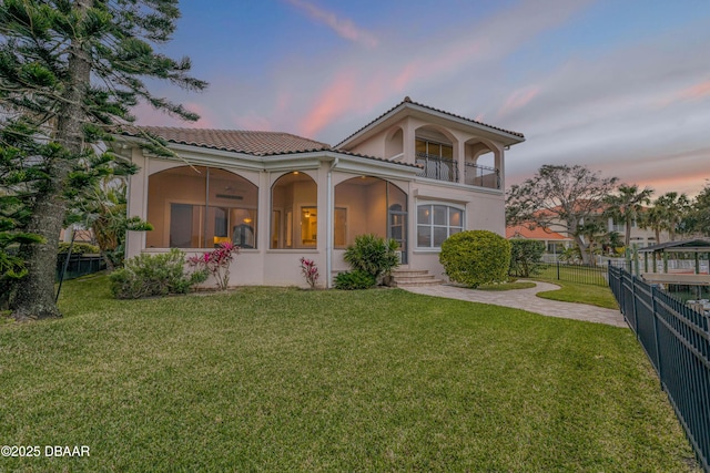 exterior space with a balcony, a tile roof, fence, a front yard, and stucco siding