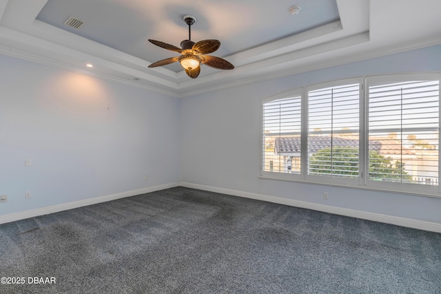 empty room featuring dark carpet, a raised ceiling, visible vents, and baseboards