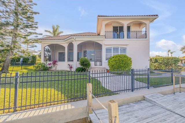 mediterranean / spanish-style home with a balcony, a tile roof, a fenced front yard, a front yard, and stucco siding