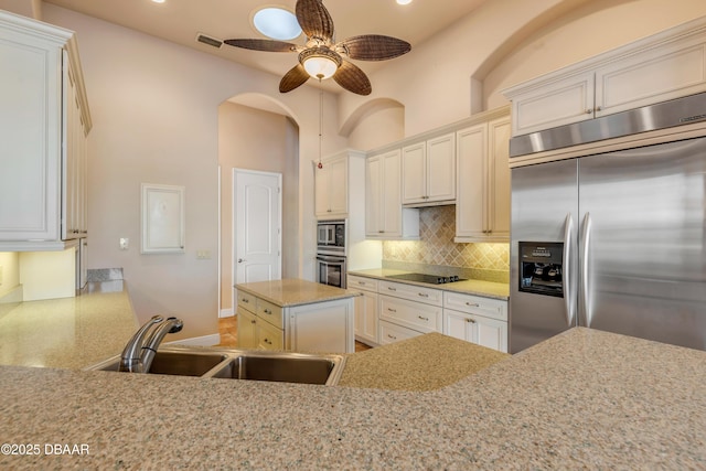 kitchen featuring built in appliances, light stone counters, a sink, visible vents, and tasteful backsplash