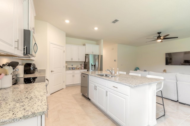kitchen with stainless steel appliances, a sink, open floor plan, a ceiling fan, and white cabinets