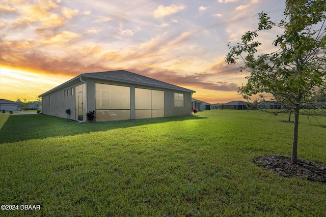 back of house at dusk with a lawn and stucco siding