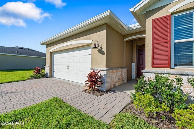 entrance to property featuring stucco siding, an attached garage, decorative driveway, and stone siding