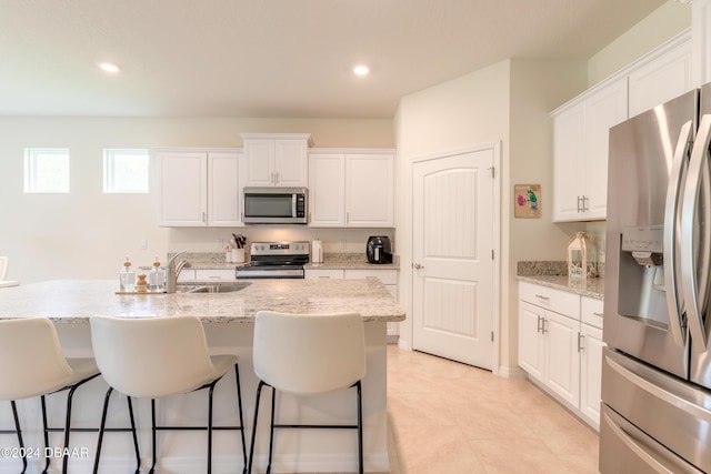 kitchen with appliances with stainless steel finishes, a sink, a breakfast bar area, white cabinets, and recessed lighting