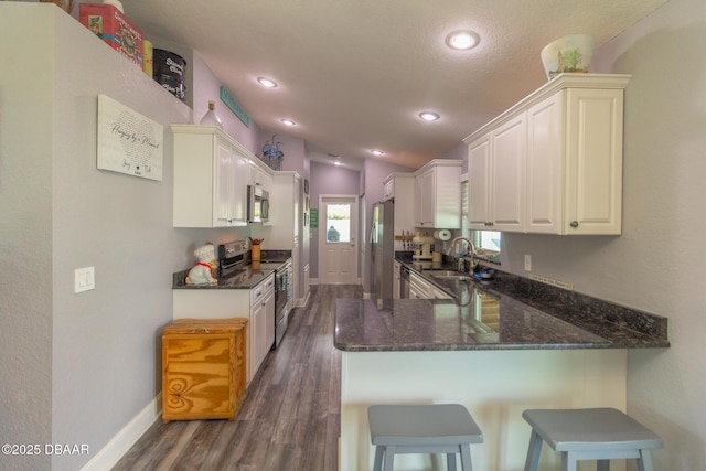 3324 Royal Palm Dr, Edgewater, FL 32141 - kitchen featuring appliances with stainless steel finishes, a peninsula, dark wood-style flooring, dark stone countertops, and a kitchen breakfast bar