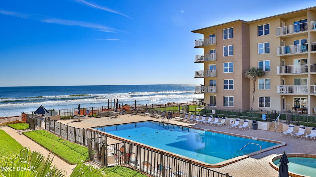 community pool featuring a beach view, fence, a water view, and a patio area