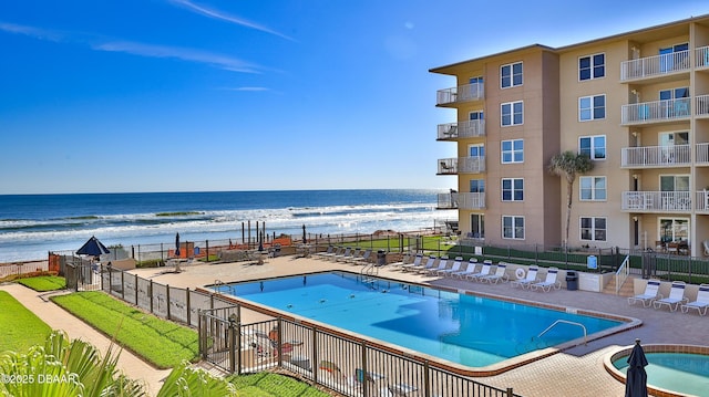 community pool featuring a beach view, fence, a water view, and a patio area