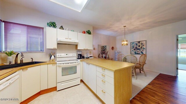 kitchen featuring light hardwood / wood-style floors, kitchen peninsula, sink, white appliances, and decorative light fixtures