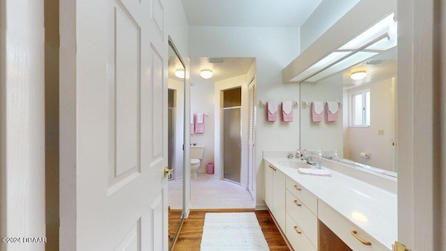 bathroom with hardwood / wood-style floors, walk in shower, vanity, and toilet