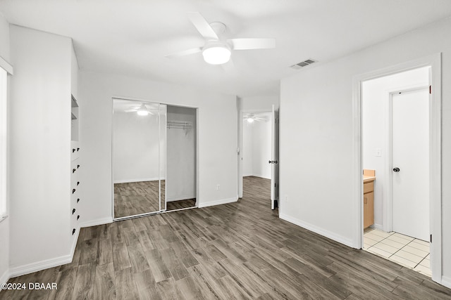 unfurnished bedroom with hardwood / wood-style floors, ceiling fan, ensuite bath, and a closet