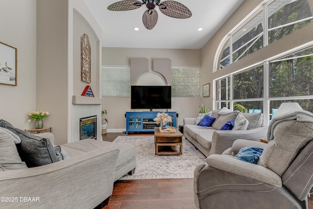 living area with wood finished floors, a ceiling fan, a glass covered fireplace, recessed lighting, and baseboards