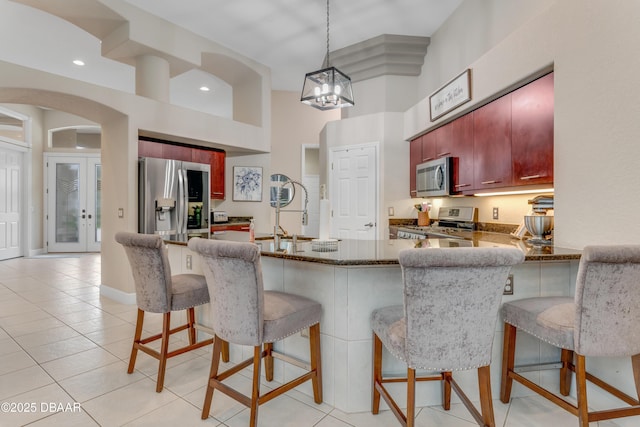 kitchen featuring appliances with stainless steel finishes, a sink, a towering ceiling, reddish brown cabinets, and a peninsula