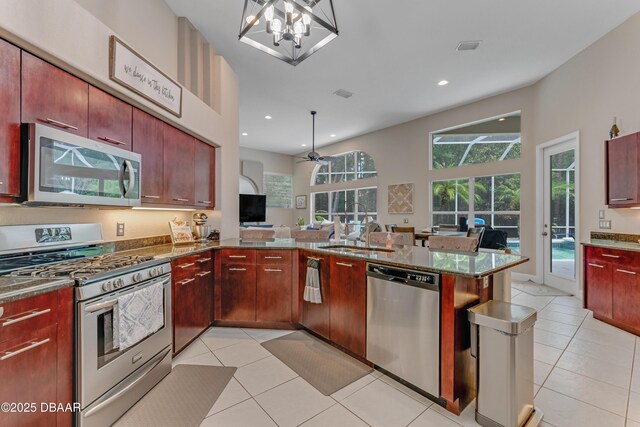 kitchen with stainless steel appliances, a sink, light tile patterned flooring, dark stone counters, and recessed lighting