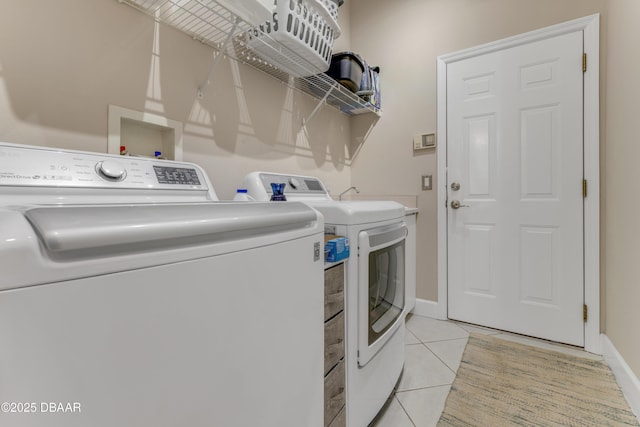 clothes washing area with washer and clothes dryer, light tile patterned flooring, and baseboards
