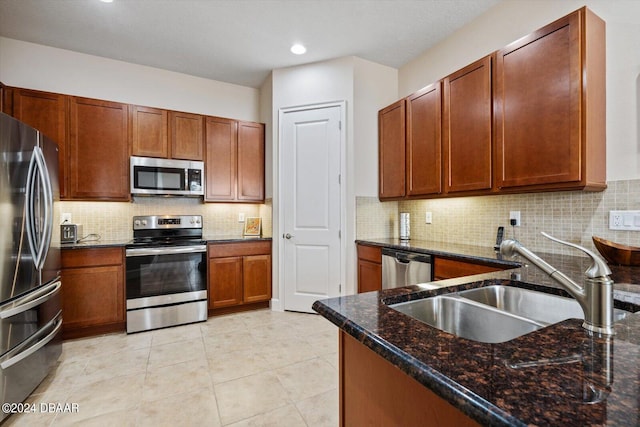 kitchen featuring stainless steel appliances, dark stone counters, decorative backsplash, sink, and light tile patterned floors