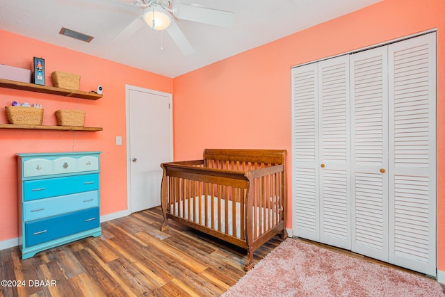 bedroom with a nursery area, dark hardwood / wood-style floors, a closet, and ceiling fan