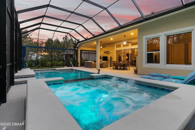 pool at dusk with an in ground hot tub, an outdoor hangout area, ceiling fan, glass enclosure, and a patio area