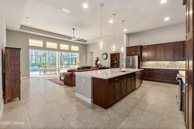 kitchen featuring sink, hanging light fixtures, a high ceiling, a kitchen island with sink, and backsplash