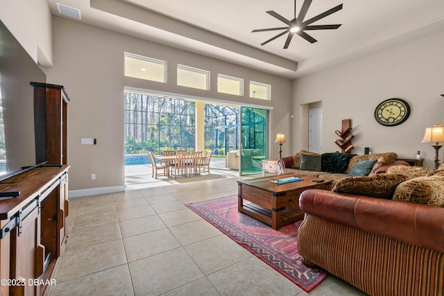 tiled living room with a towering ceiling, a raised ceiling, and ceiling fan